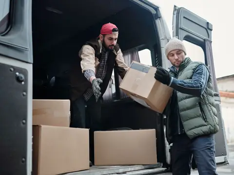 Two workers loading cardboard boxes into the back of a van