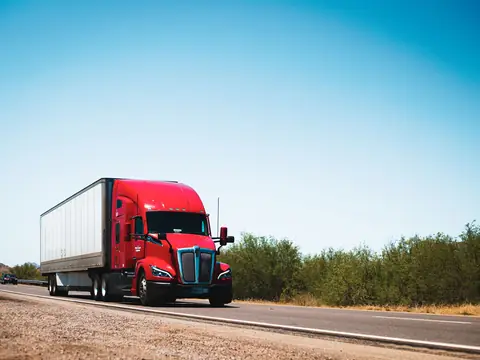 A red semi truck driving on an open highway under a clear blue sky