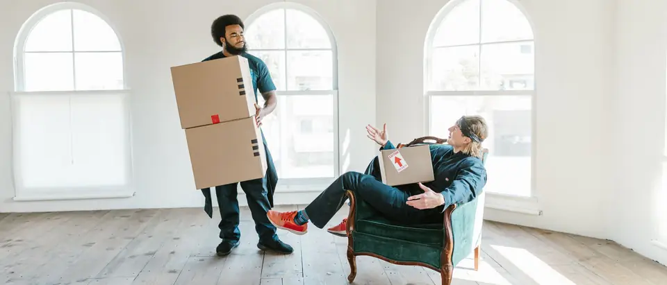 Two movers with moving boxes in a bright empty room with arched windows
