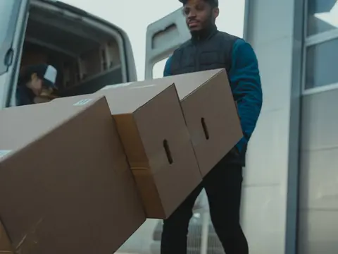 A worker carrying cardboard boxes from an open van