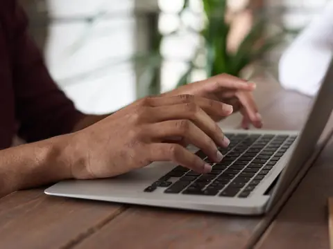 Hands typing on a laptop at a wooden table