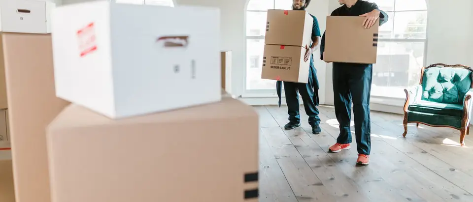 Two movers in uniform carrying boxes into a bright new home