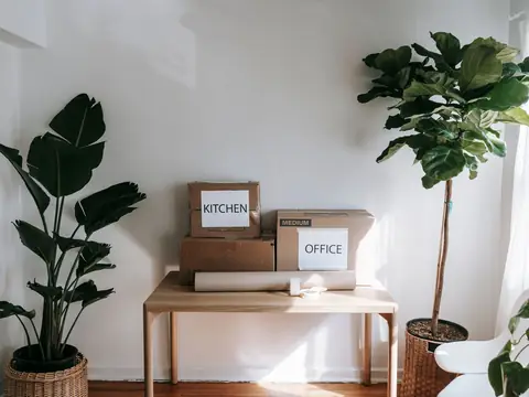 Moving boxes labeled Kitchen and Office on a wooden table in a bright apartment