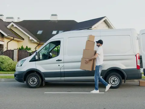 A man carrying boxes from a white van parked in front of a house