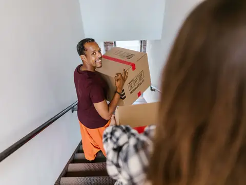 A mover carrying a moving box up an indoor staircase