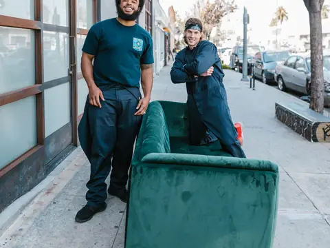 Two movers with a green sofa on a sunny city sidewalk