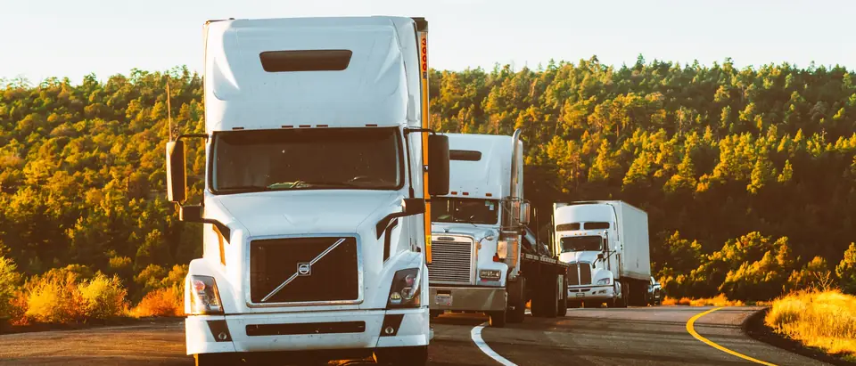 Three semi trucks driving on a highway through a forest in Arizona