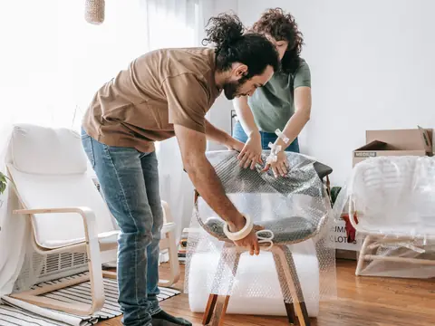 A couple wrapping a chair in bubble wrap in their apartment