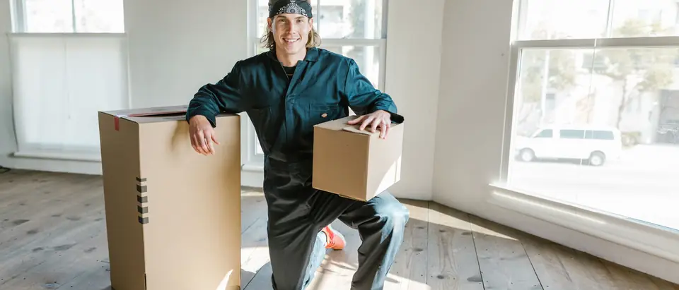 A mover in a coverall kneeling beside moving boxes in a sunlit apartment