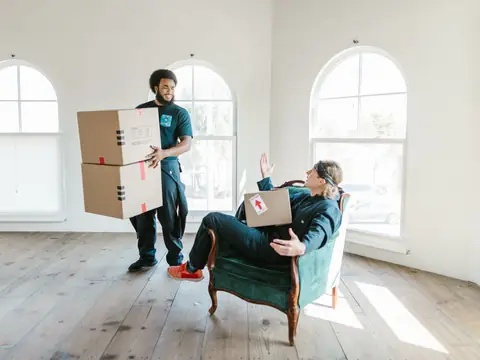 Two movers handling cardboard boxes in a bright room with large windows