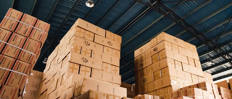High stacks of cardboard boxes in a warehouse under a blue metal roof
