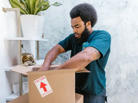 A mover packing a fragile item into a box in a bright room
