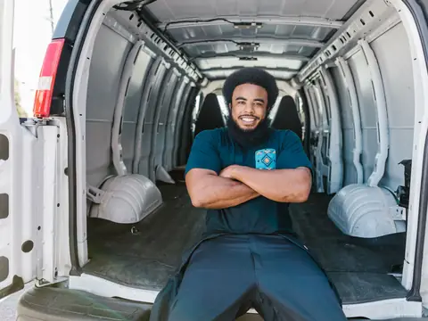 A smiling mover sitting with folded arms in the back of an empty moving van